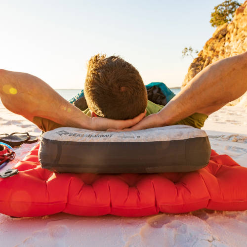 Ein Mann liegt auf einer Isomatte am Strand